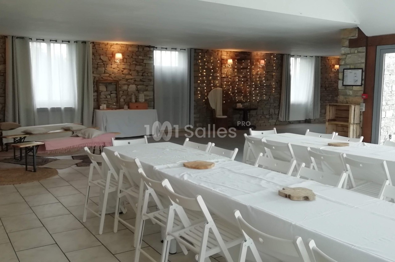 Salle de réception avec murs en pierre, tables blanches dressées et guirlandes lumineuses en arrière-plan.