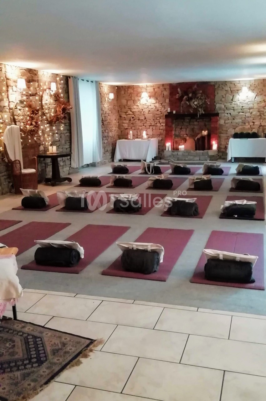 Salle aménagée pour une séance de méditation avec des tapis et coussins alignés sur un sol en pierre, éclairage tamisé.