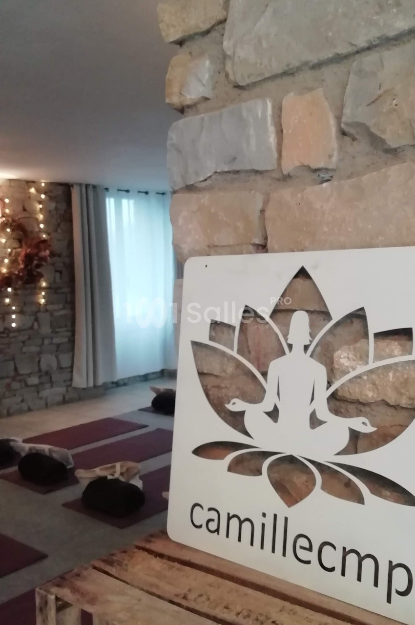 Salle de yoga avec tapis au sol, mur en pierre, lumière tamisée et panneau décoratif en forme de lotus.