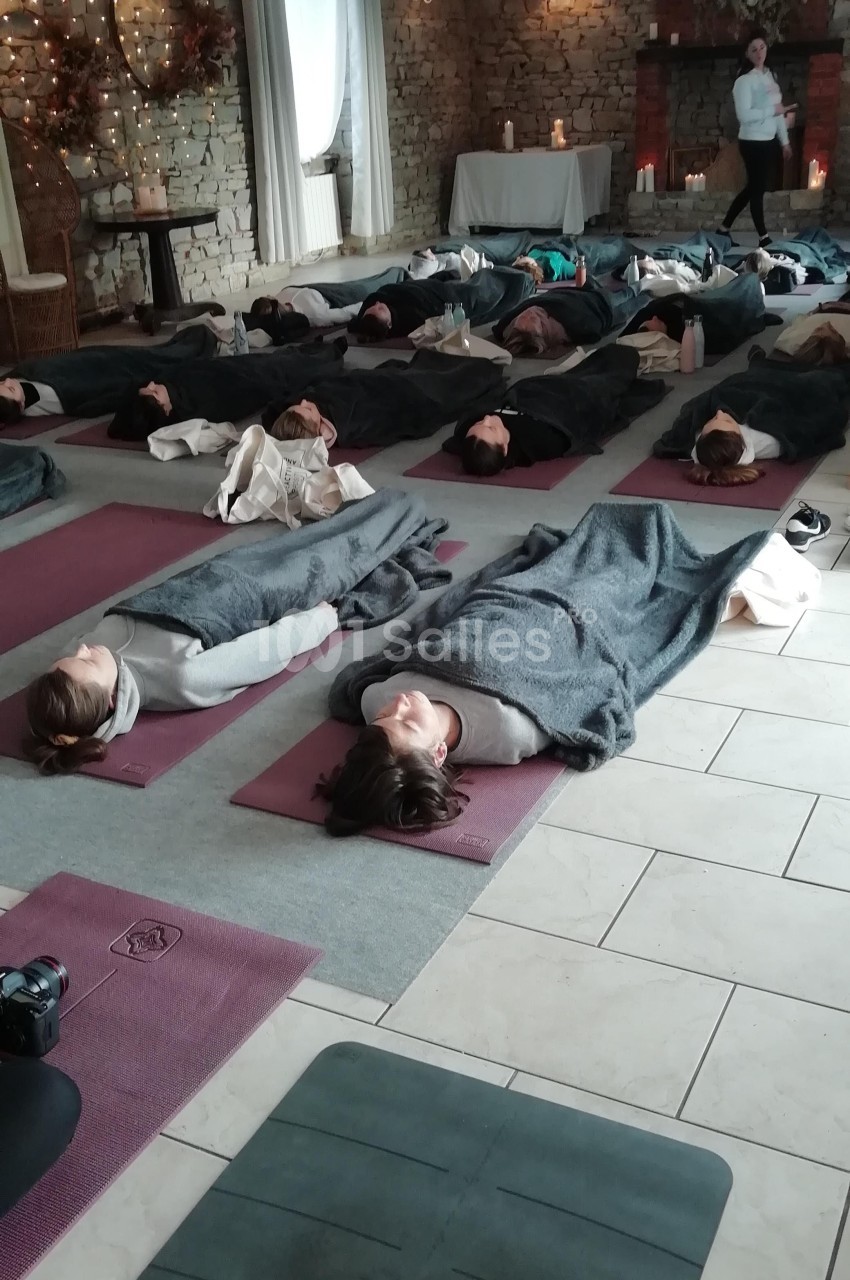Personnes allongées sur des tapis de yoga, couvertes de couvertures, dans une salle éclairée de manière tamisée.