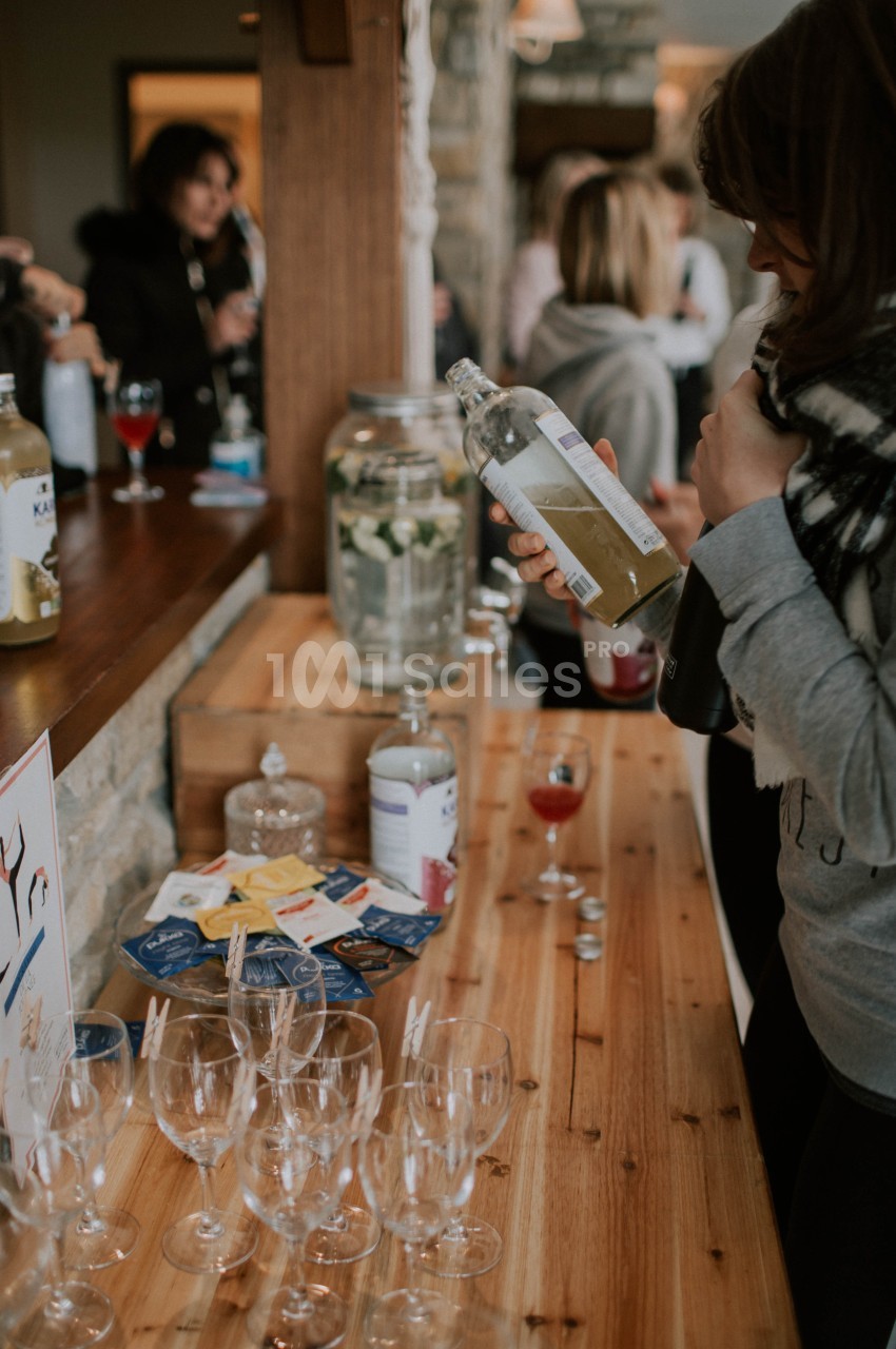 Une femme verse une boisson dans un verre sur un comptoir en bois, entourée de verres et de sachets de thé.