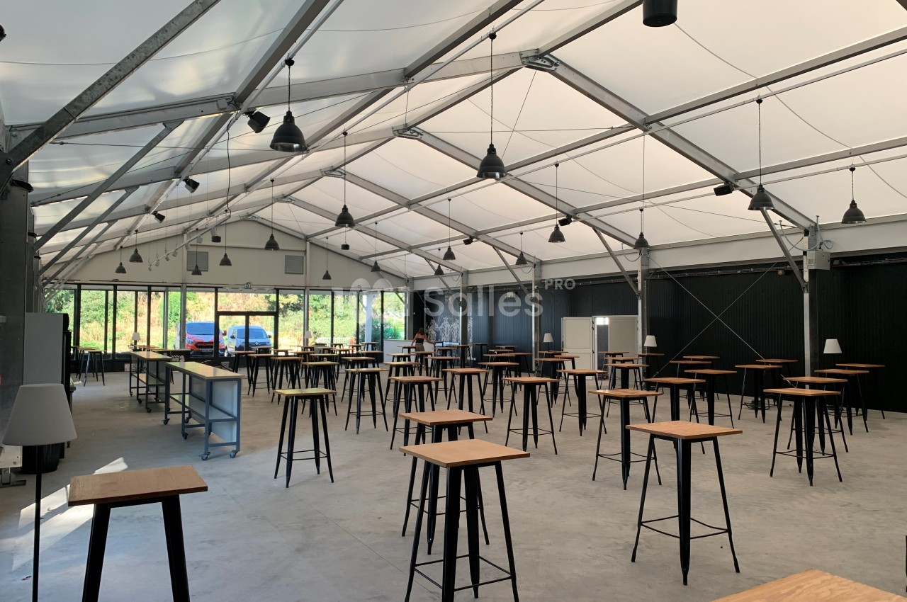 Intérieur d'une grande structure en toile avec des tables hautes en bois et des luminaires suspendus.