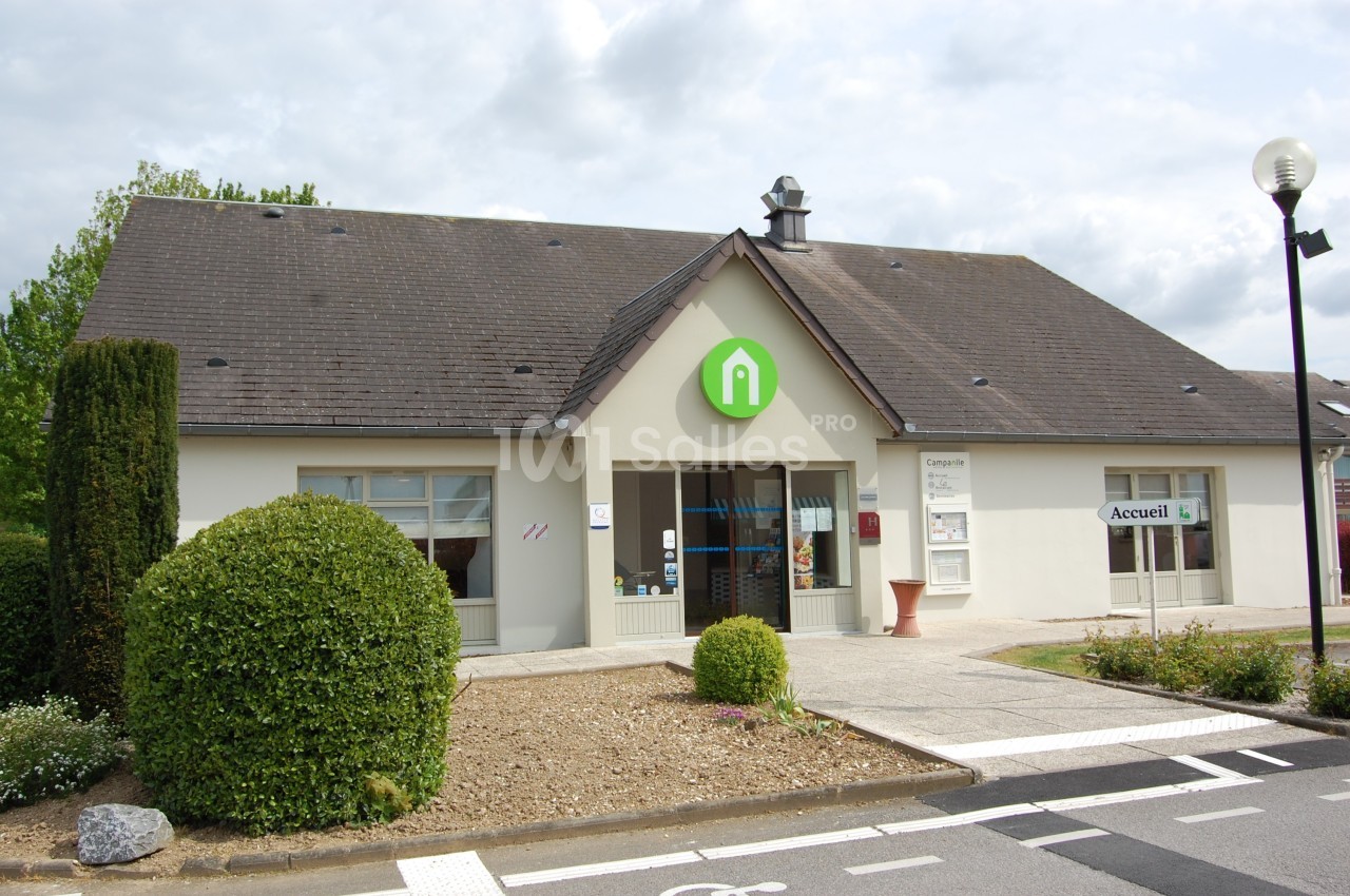 Bâtiment avec toit en ardoise, entrée principale vitrée et panneau vert affichant un logo en forme de maison.