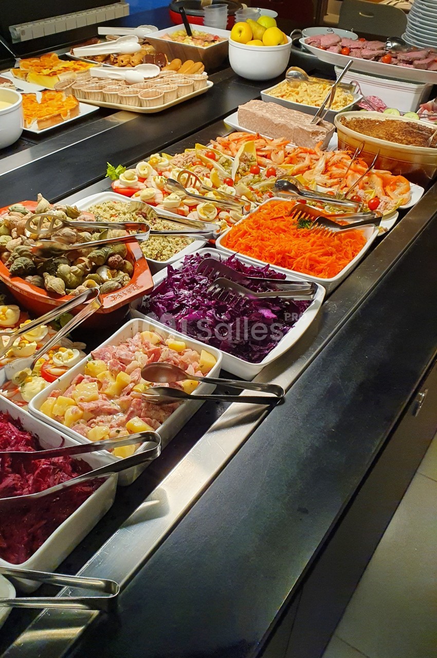 Buffet varié avec salades, légumes, charcuteries et condiments disposés dans des plats sur un comptoir.
