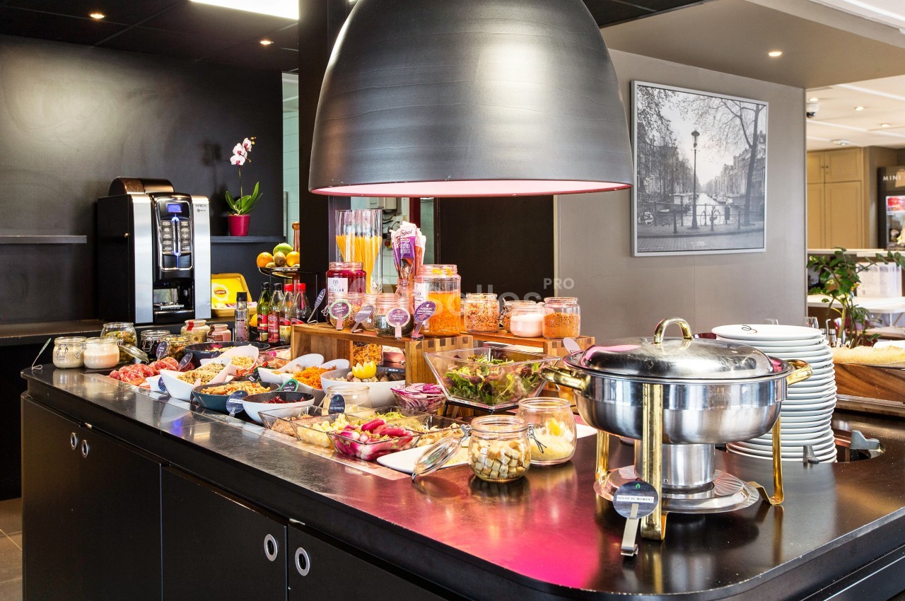 Buffet de petit-déjeuner avec plats variés, fruits, céréales, viennoiseries et boissons dans un espace moderne.