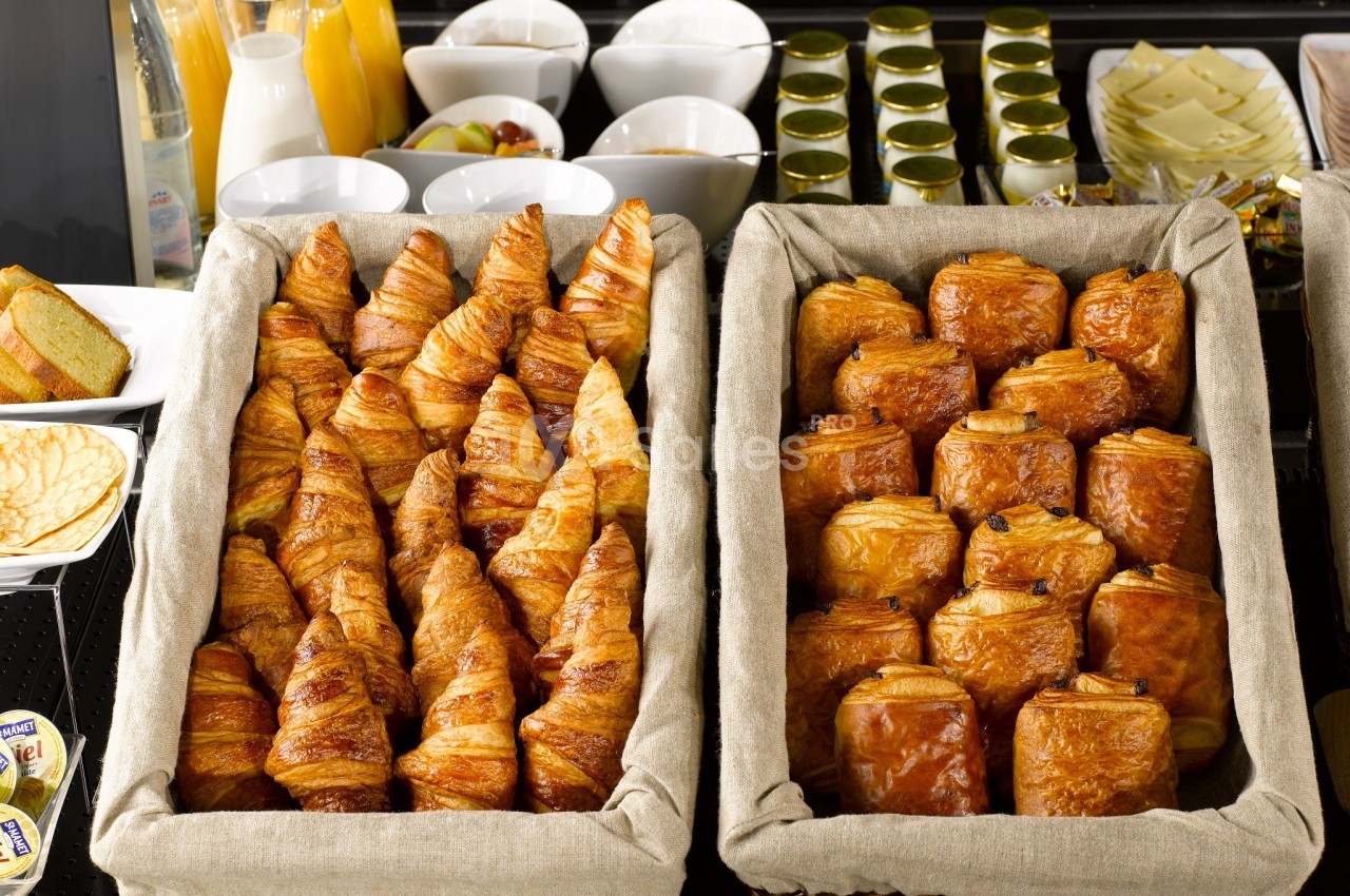 Paniers garnis de croissants et pains au chocolat sur un buffet avec boissons et condiments en arrière-plan.