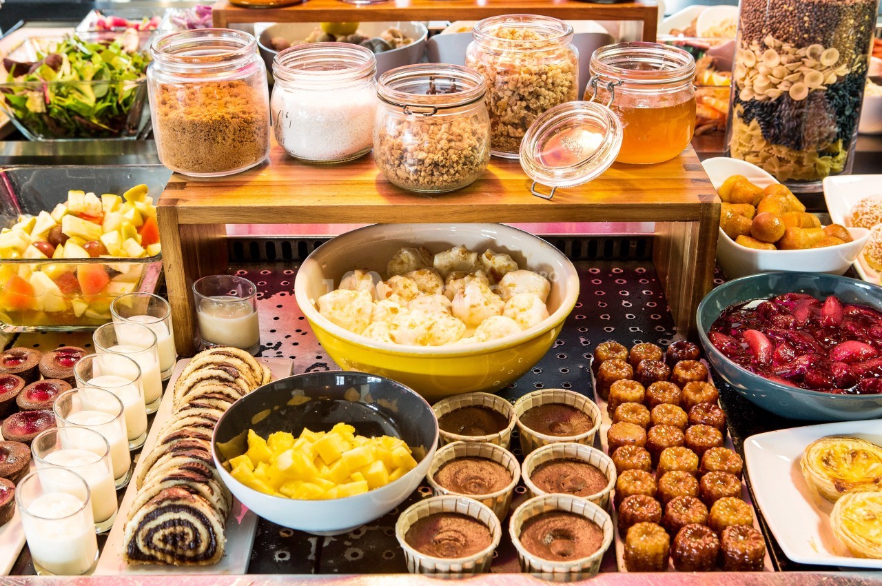 Buffet de desserts variés avec fruits, pâtisseries, yaourts, confitures et céréales présentés dans des bols et des pots.