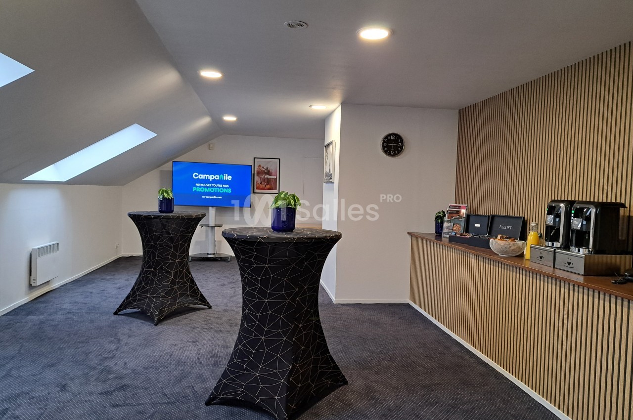 Salle de réunion avec tables hautes, écran allumé, horloge murale et coin café sur un meuble en bois.