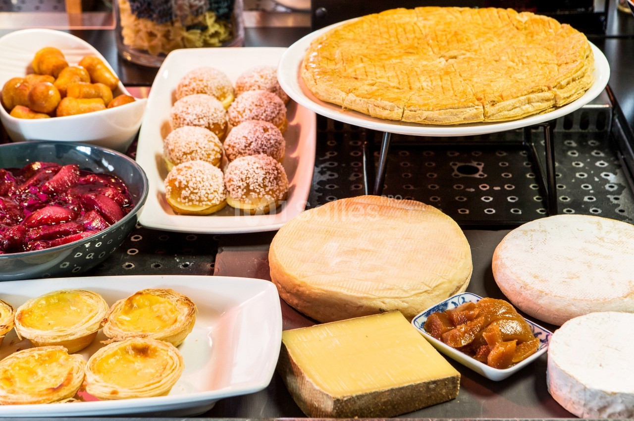 Assortiment de desserts et fromages présentés sur un buffet, incluant tartes, fromages et pâtisseries variées.