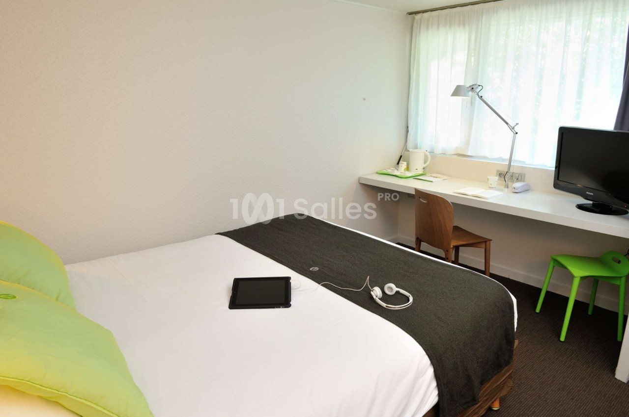 Chambre d'hôtel lumineuse avec un lit double, un bureau équipé d'une lampe, une chaise et une télévision.