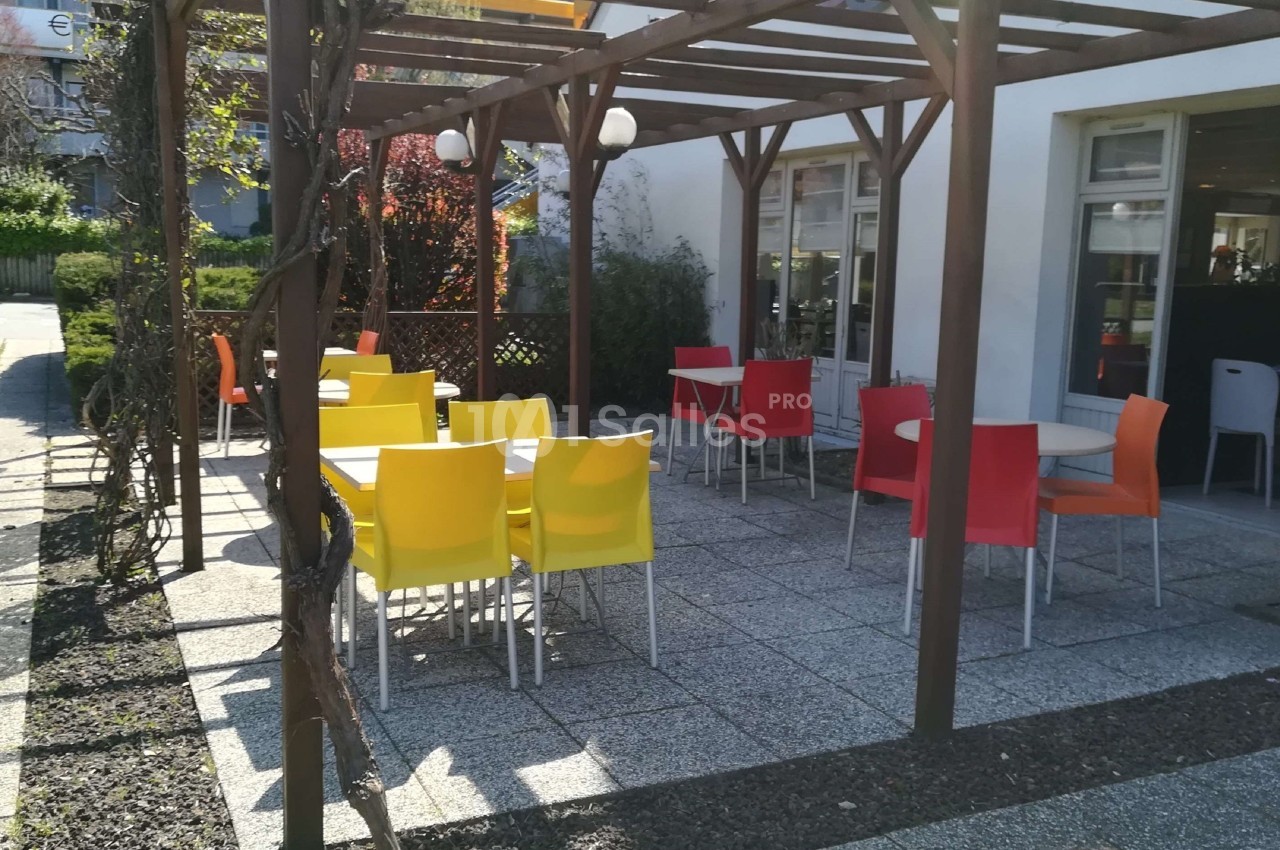 Terrasse extérieure avec tables et chaises colorées sous une pergola en bois, près d'un bâtiment vitré.