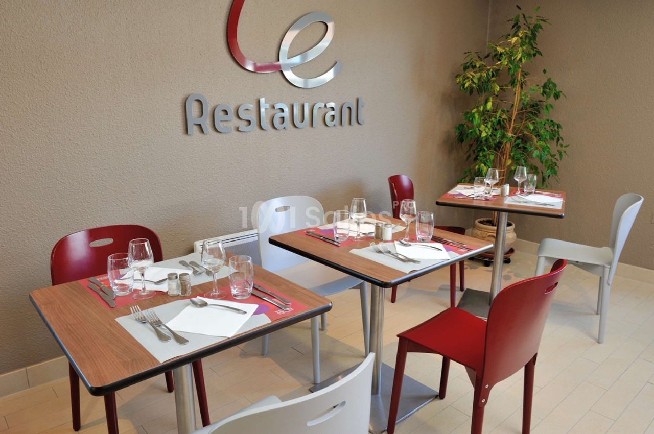 Salle de restaurant avec tables dressées, chaises colorées et décoration sobre, incluant une plante verte.