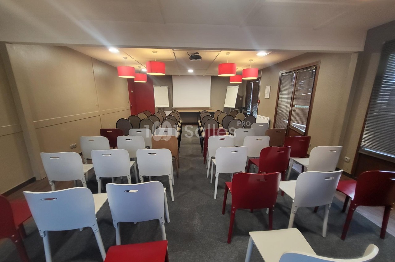 Salle de conférence avec des rangées de chaises colorées face à un écran de projection et deux tableaux blancs.