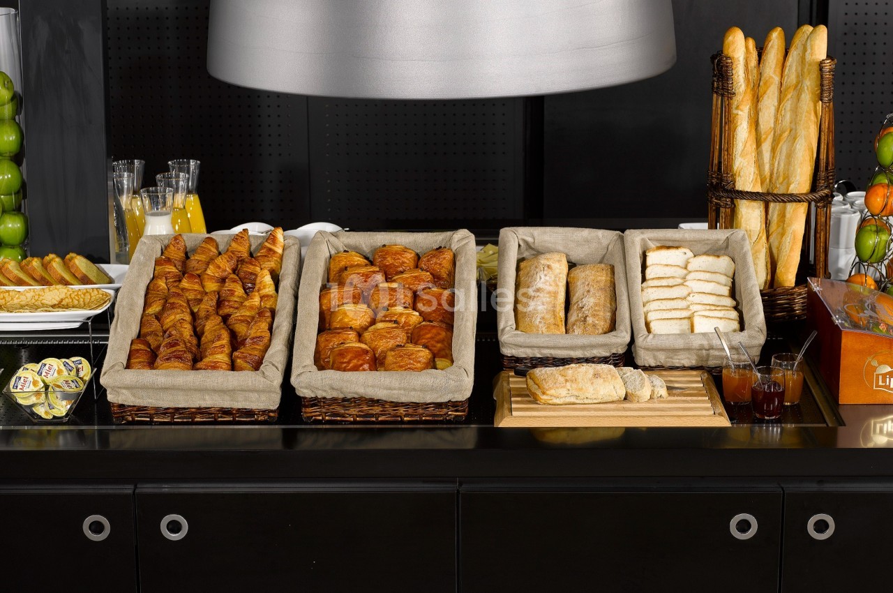 Buffet de viennoiseries et pains variés disposés dans des paniers en tissu sur un comptoir noir.