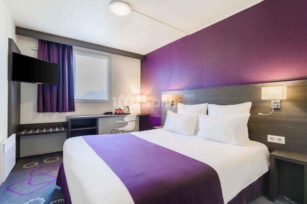 Chambre d'hôtel avec lit double, mur violet, bureau, télévision murale et éclairage doux.