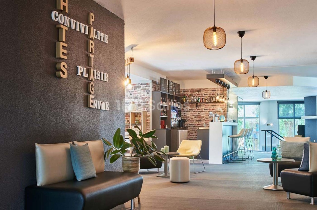 Salon moderne avec canapés, plantes, éclairage suspendu et bar en arrière-plan dans une ambiance conviviale.