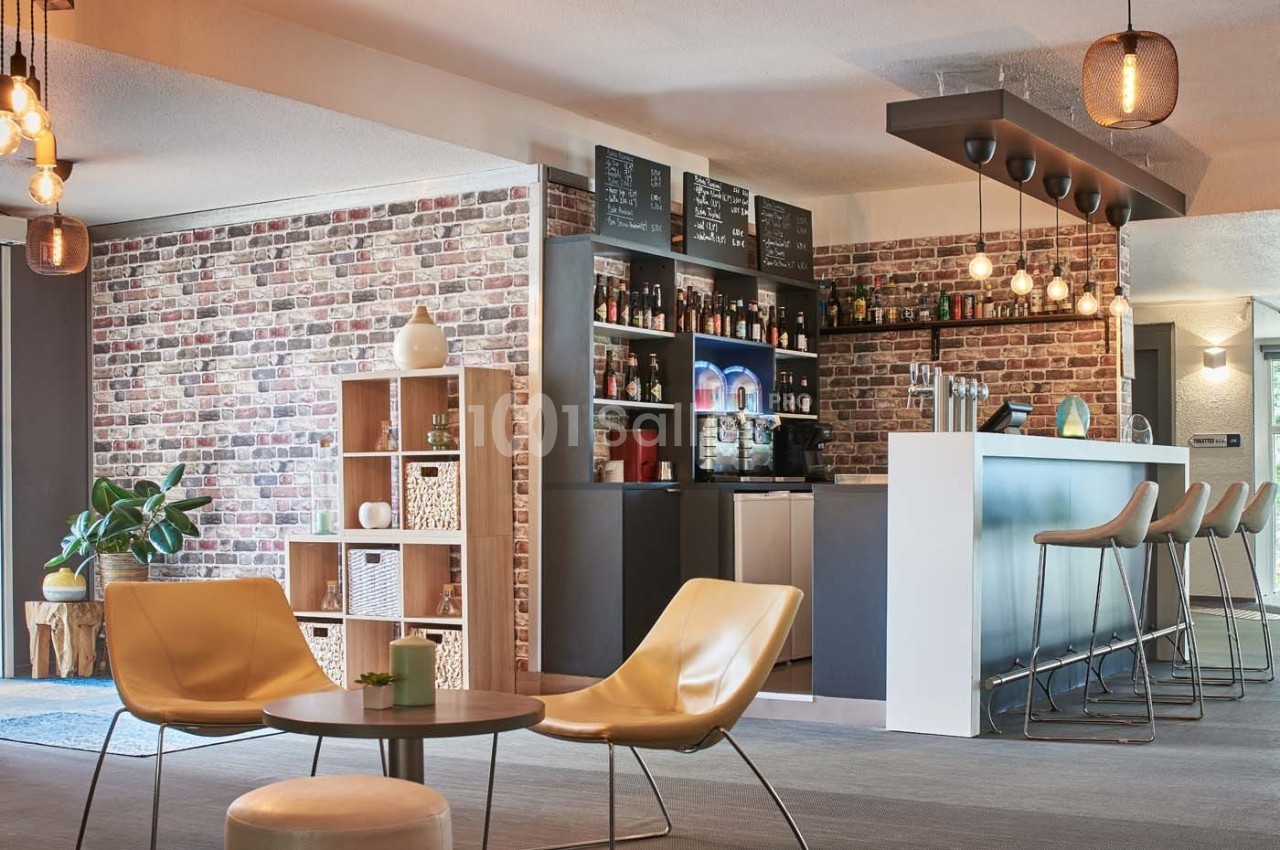 Espace bar moderne avec comptoir, tabourets hauts, étagères décoratives et mur en briques apparentes.