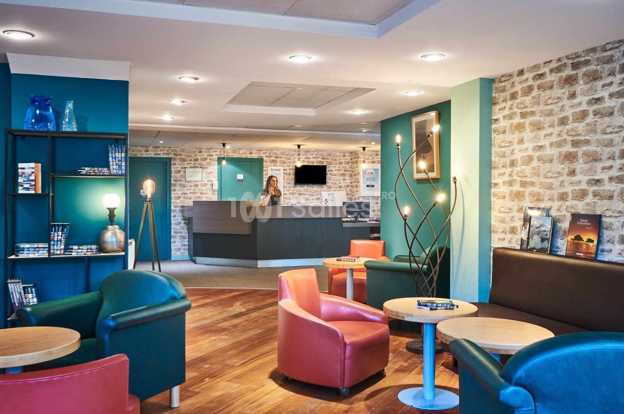 Espace d'accueil lumineux avec comptoir de réception, fauteuils colorés, tables basses et murs en pierre apparente.
