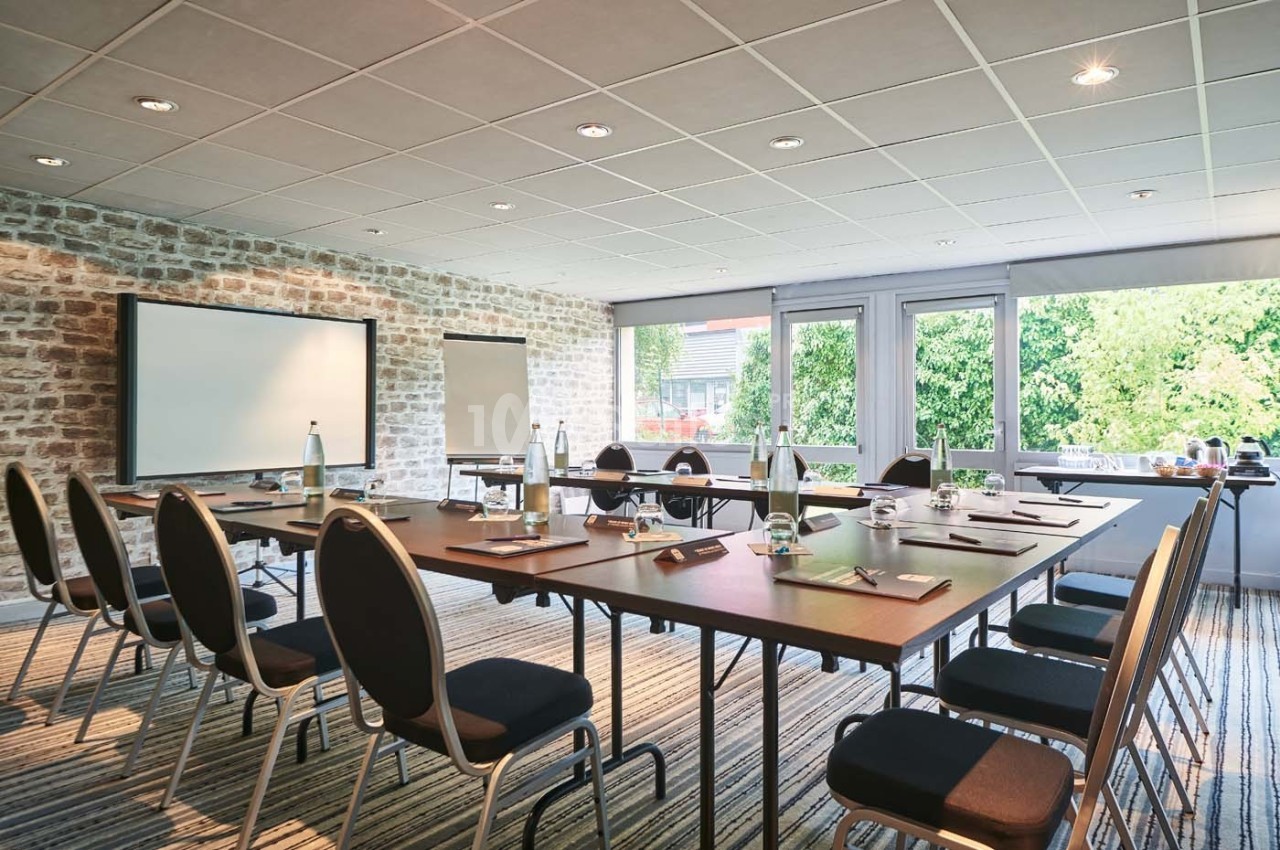 Salle de réunion lumineuse avec table rectangulaire, chaises, tableau blanc, paperboard et vue sur un espace vert.