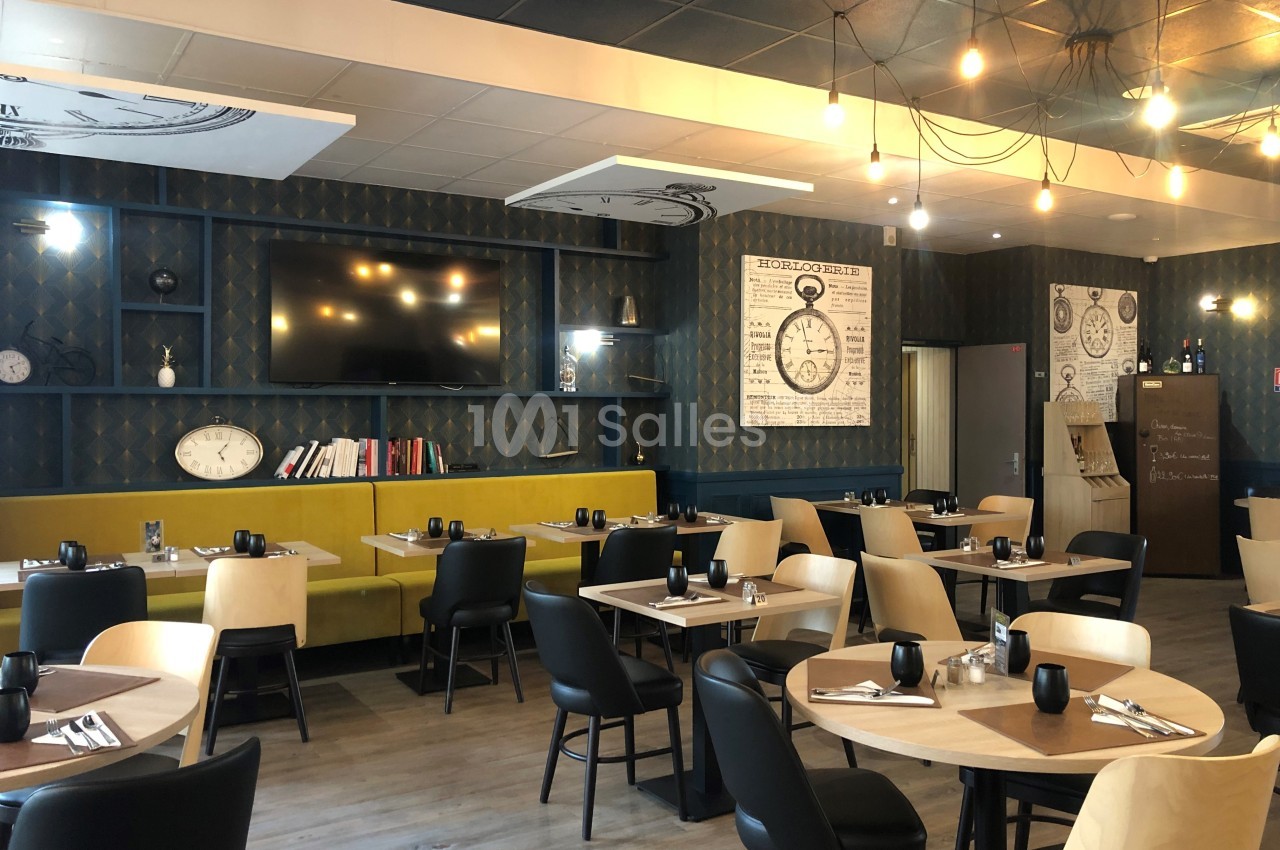 Salle de restaurant moderne avec tables dressées, chaises en bois et banquettes, éclairage suspendu et décoration murale.