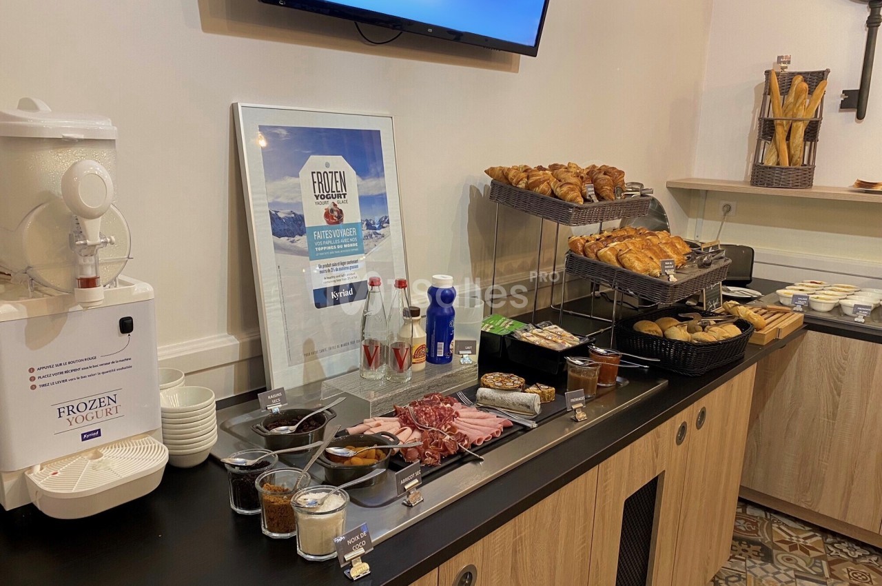 Buffet de petit-déjeuner avec viennoiseries, pains, charcuterie, yaourt glacé, boissons et condiments sur un comptoir.