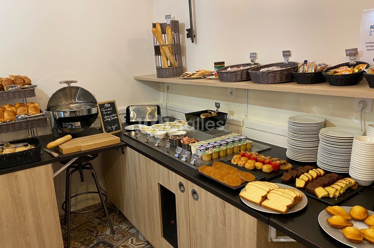 Buffet de petit-déjeuner avec pains, viennoiseries, yaourts, fruits, confitures et boissons disposés sur un comptoir.
