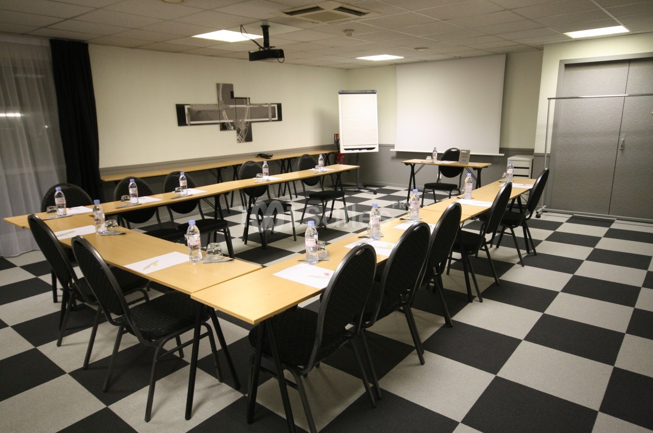Salle de réunion avec tables disposées en U, chaises, bouteilles d'eau, bloc-notes et écran de projection.