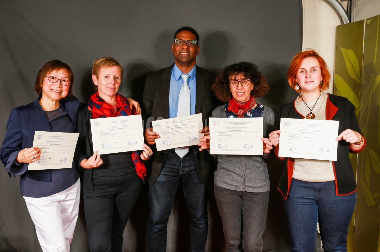 Cinq personnes debout tenant des certificats, posant devant un fond sombre dans un cadre formel.