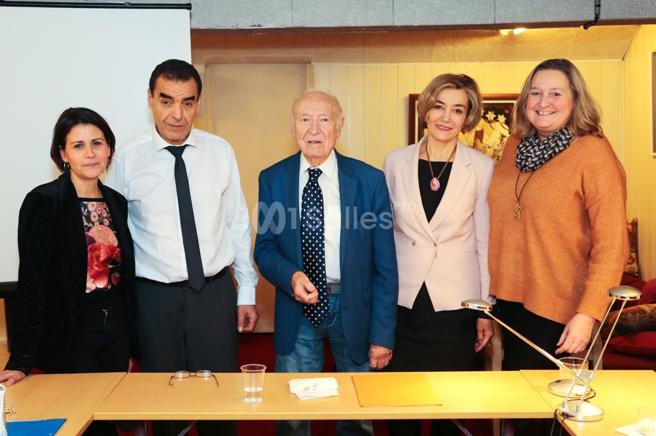 Cinq personnes debout derrière une table dans une salle, posant pour une photo de groupe.