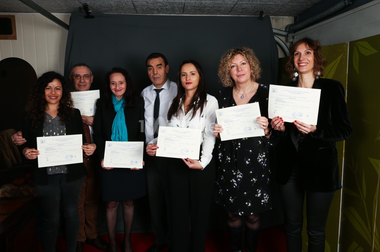 Un groupe de sept personnes pose avec des certificats dans un cadre intérieur devant un fond sombre.