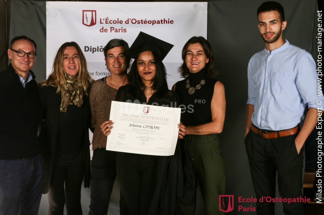 Un groupe de six personnes pose avec une diplômée tenant son certificat devant une bannière d'école d'ostéopathie.