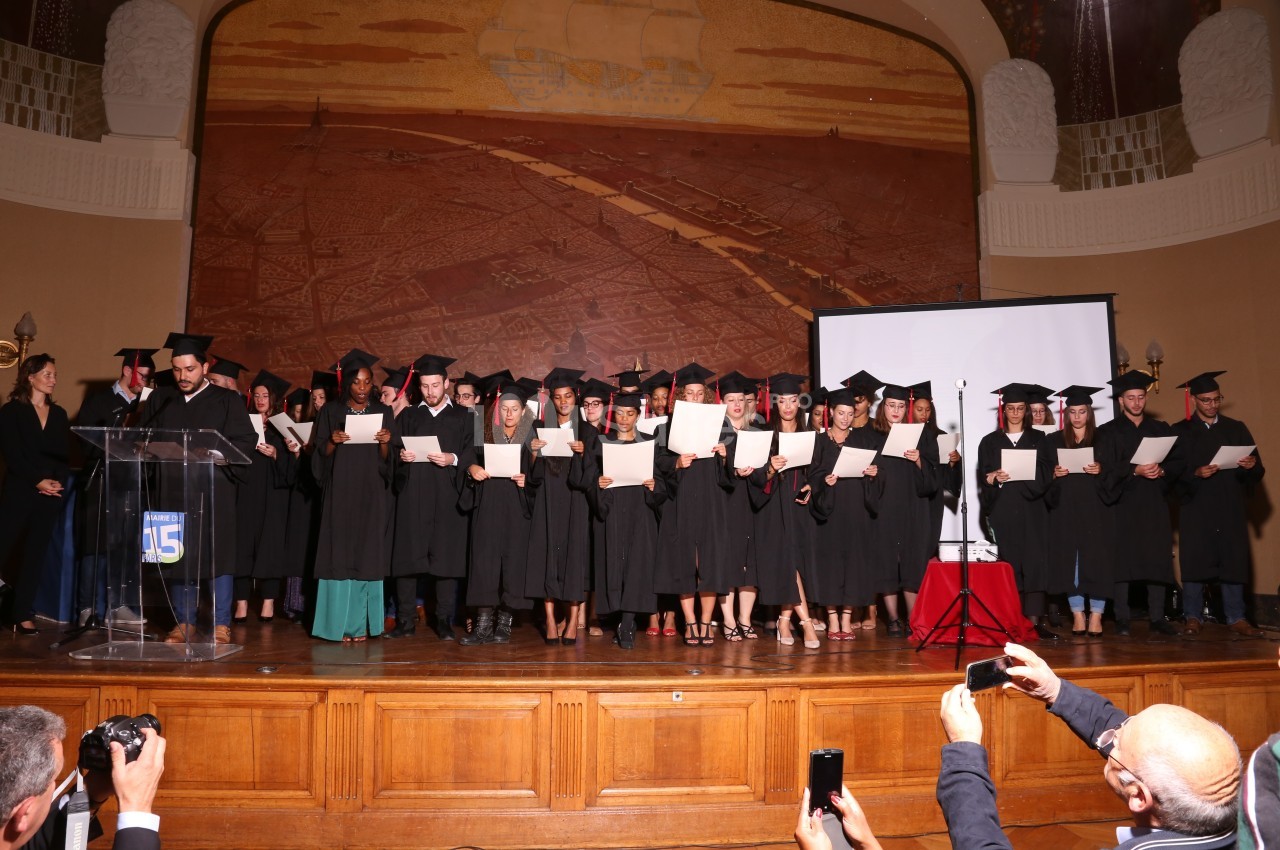 Un groupe de diplômés en toges et coiffés de mortiers posant sur une scène avec leurs diplômes.
