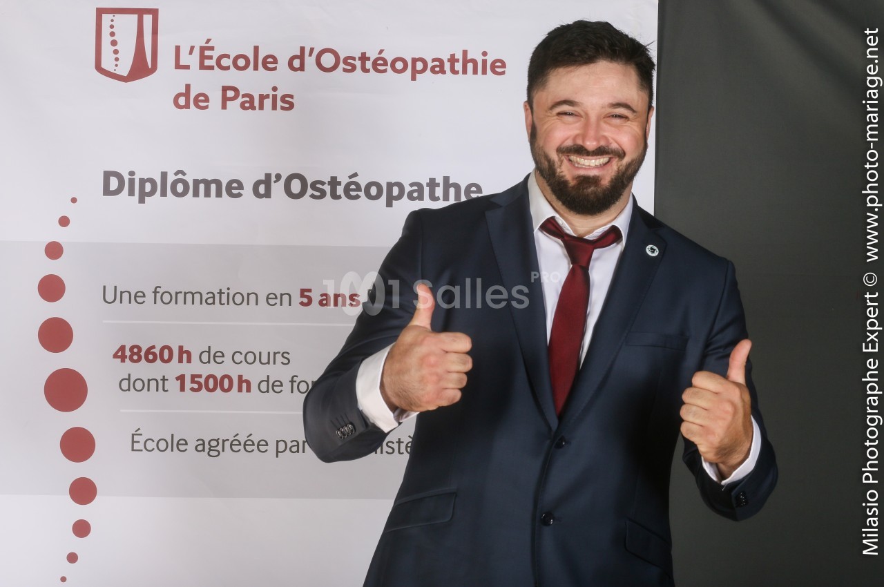 Homme souriant en costume, levant les pouces devant une affiche de l'École d'Ostéopathie de Paris.