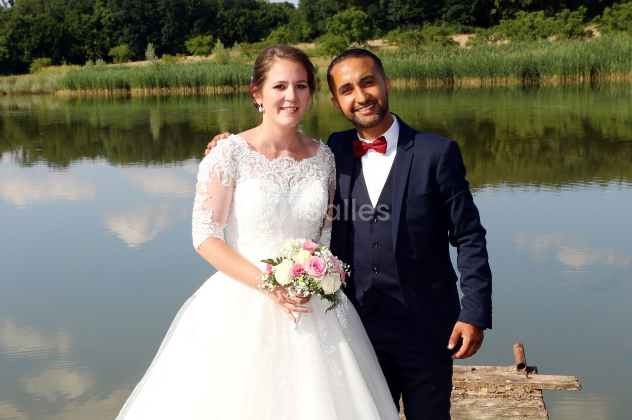 Un couple en tenue de mariage pose devant un lac entouré de végétation.