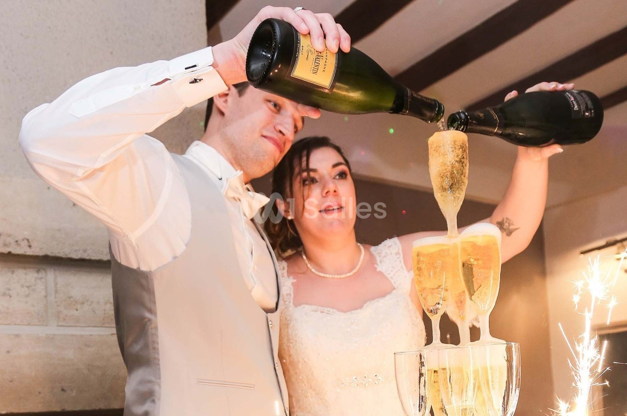 Un couple en tenue de mariage verse du champagne dans une fontaine de verres empilés.