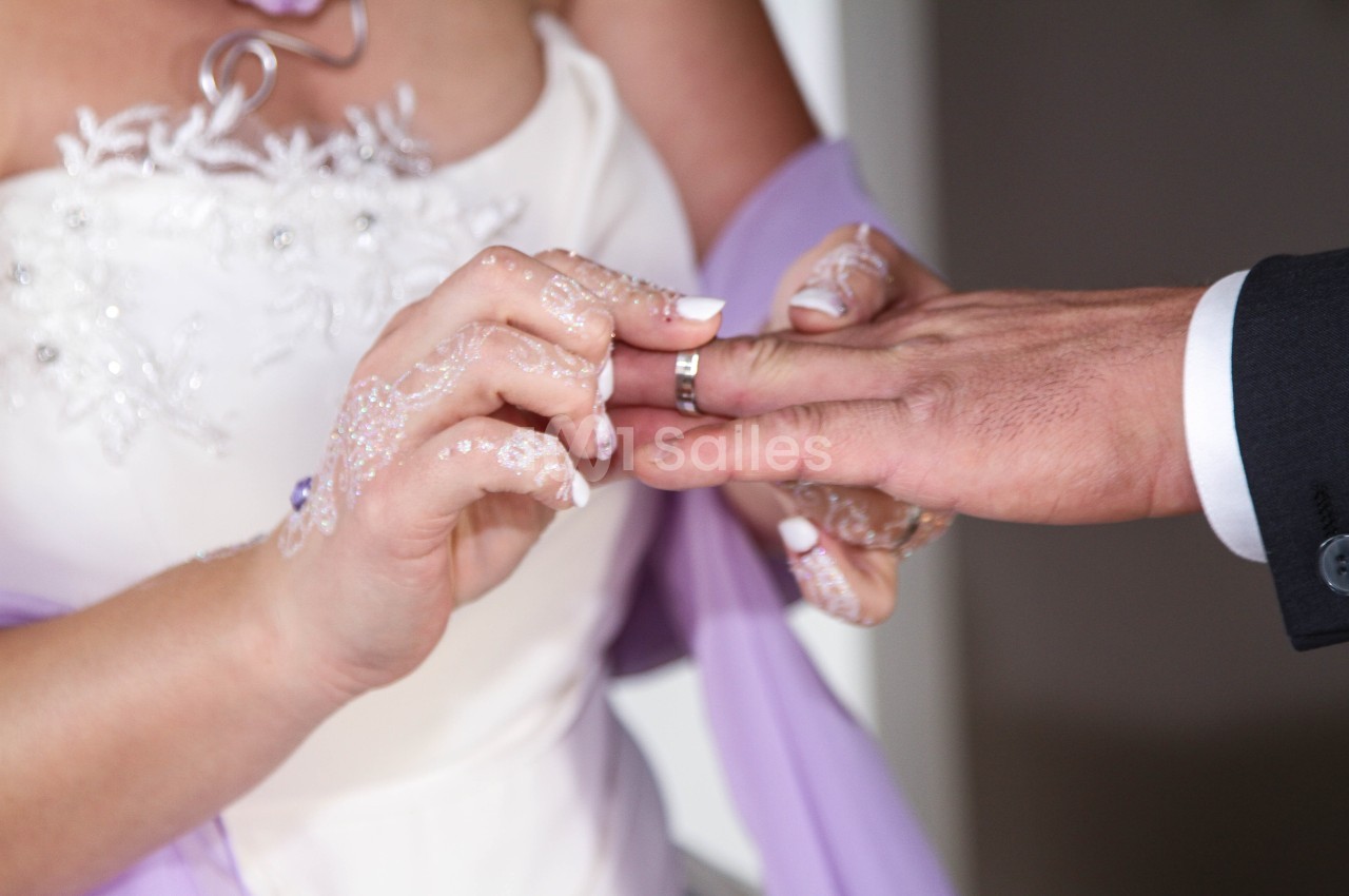 Une mariée passe une alliance au doigt d'un homme, symbolisant un échange de vœux lors d'une cérémonie de mariage.