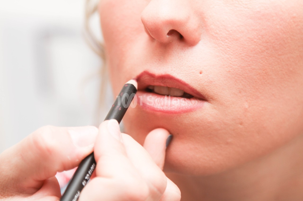 Application de crayon à lèvres sur les contours de la bouche d'une femme par une main visible.
