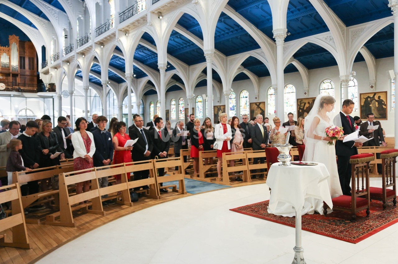 Un couple se tient debout devant l'autel lors d'une cérémonie de mariage dans une église remplie d'invités.