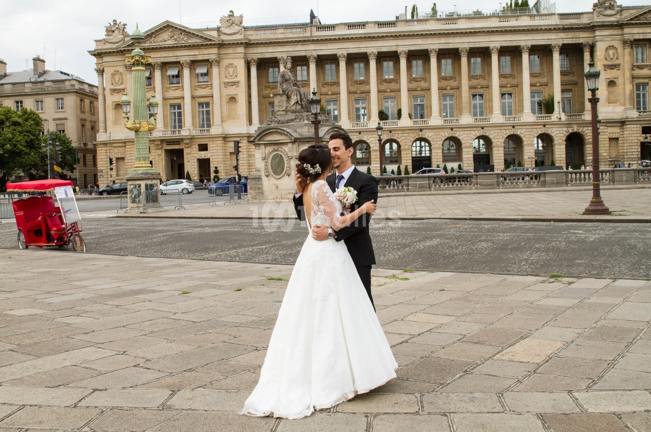 Un couple en tenue de mariage danse sur une place pavée devant un bâtiment historique.