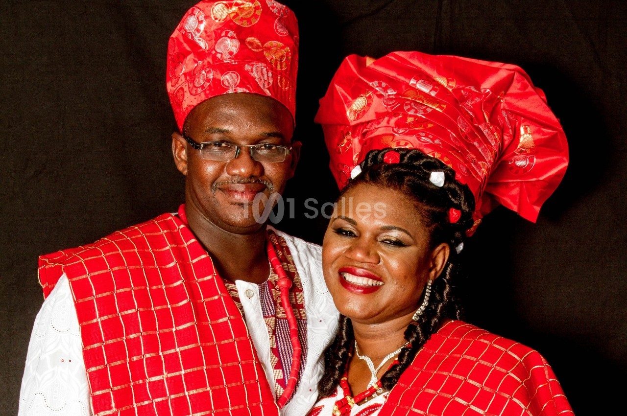 Un couple souriant portant des vêtements traditionnels rouges et blancs sur un fond sombre.