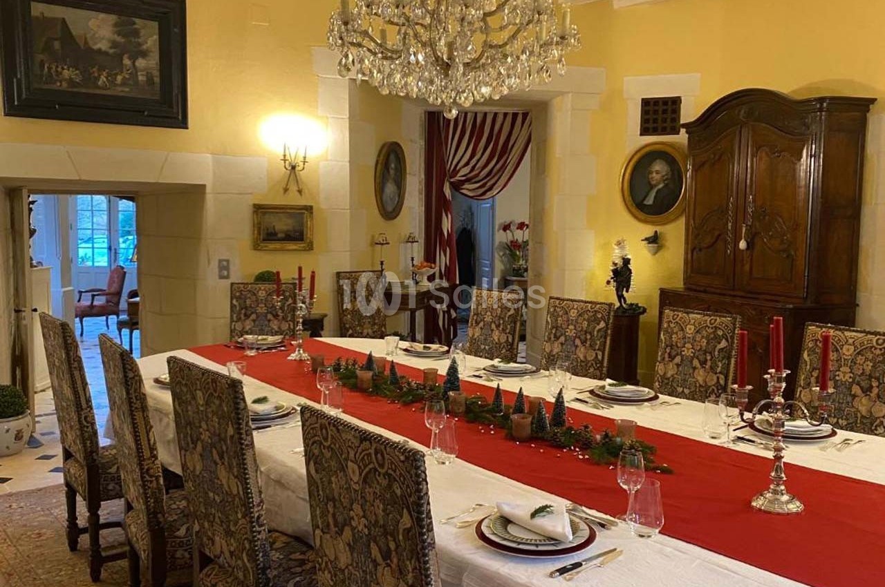 Salle à manger élégante avec une grande table dressée, nappe blanche, chemin de table rouge et chandeliers.