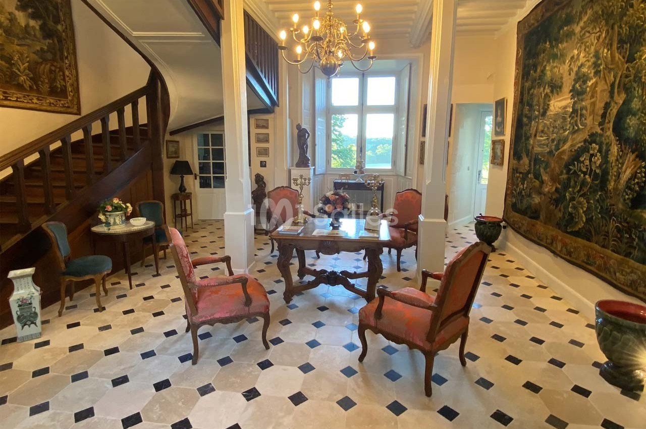Salle élégante avec mobilier ancien, tapisseries murales, sol en damier et escalier en bois dans un intérieur lumineux.
