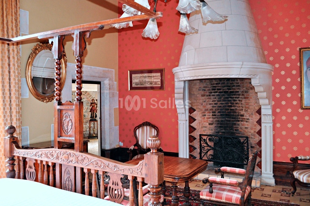 Chambre avec lit en bois sculpté, cheminée en pierre, murs rouges décorés et mobilier ancien.