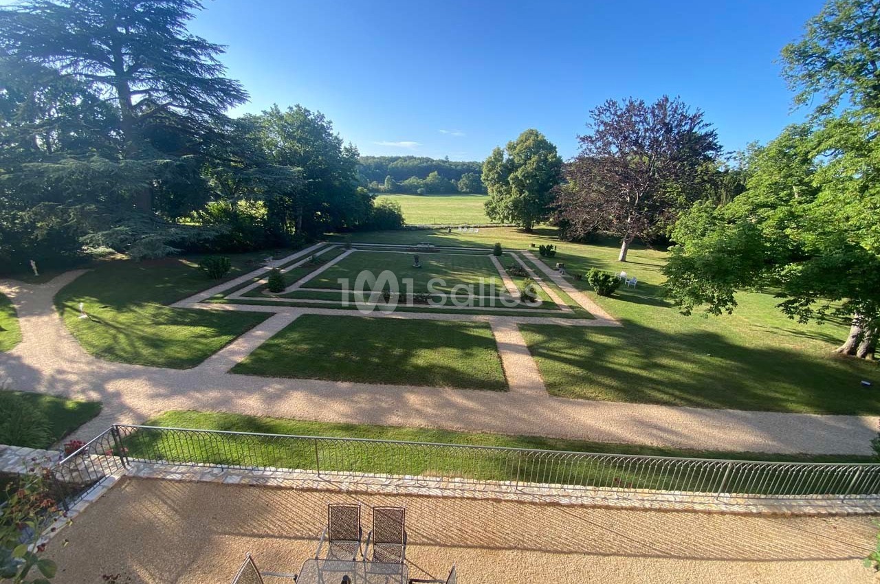 Vue d'un jardin paysager avec allées gravillonnées, pelouses, parterres fleuris et arbres sous un ciel dégagé.