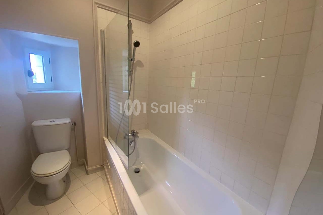 Salle de bain avec baignoire, paroi vitrée, carrelage blanc et petite fenêtre laissant entrer la lumière naturelle.