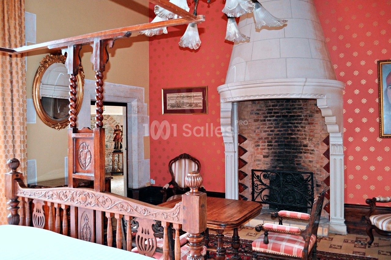 Chambre avec lit en bois sculpté, cheminée en pierre, murs rouges décorés et mobilier ancien.