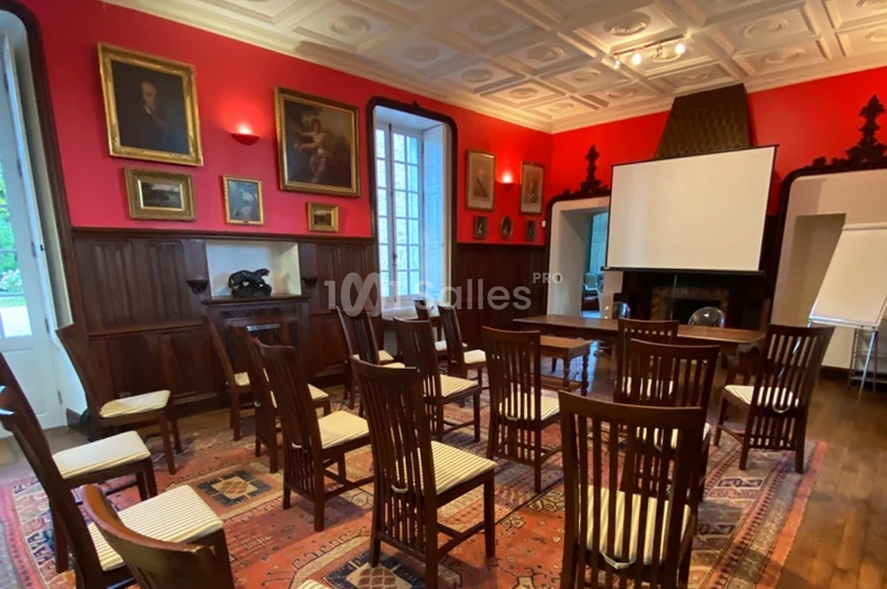 Salle de réunion avec des chaises en bois alignées, un écran de projection et des murs décorés de tableaux.