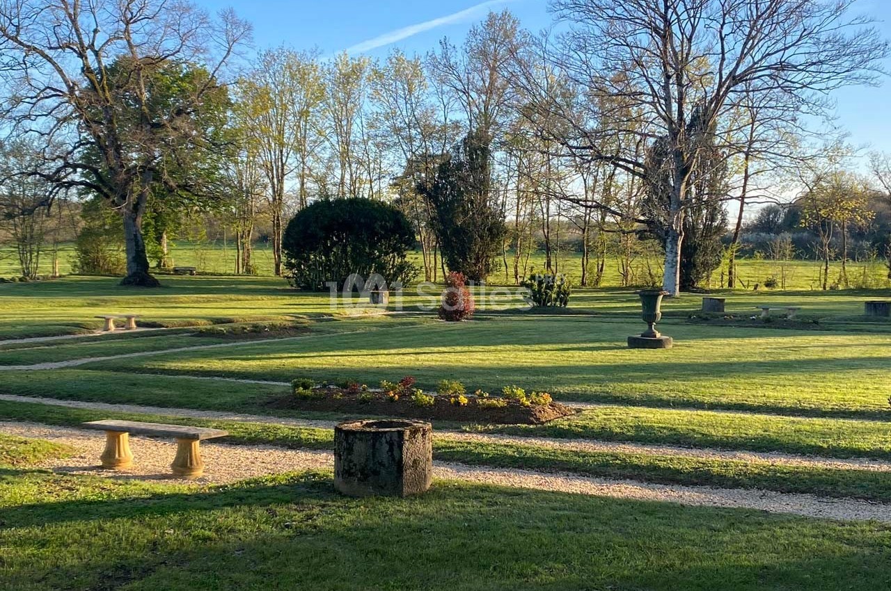 Jardin paysager avec pelouse, allées gravillonnées, arbustes taillés et arbres dénudés sous un ciel dégagé.