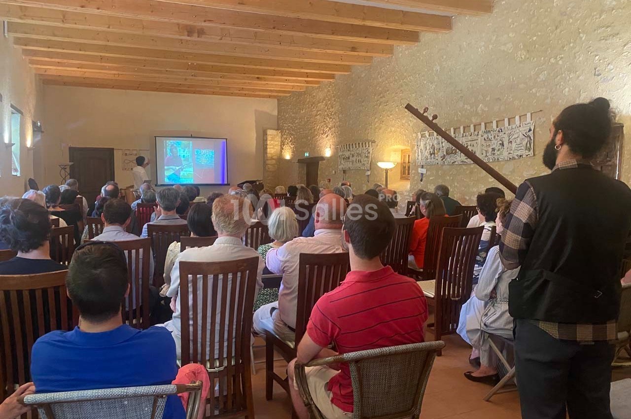 Un groupe de personnes assises dans une salle en pierre, regardant une présentation projetée sur un écran.