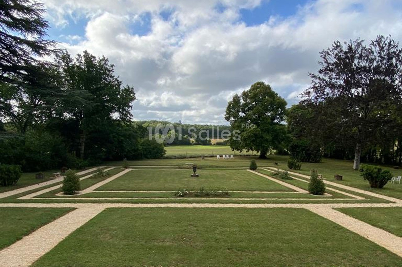 Vue d'un jardin symétrique avec pelouses, allées gravillonnées et arbres, sous un ciel partiellement nuageux.